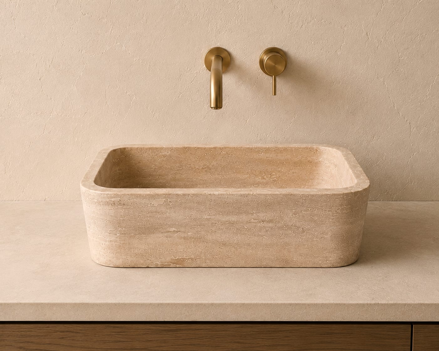 Lavabo en travertin 38x50x14 cm vu de face sur un plan en pierre claire, avec deux robinets muraux en laiton