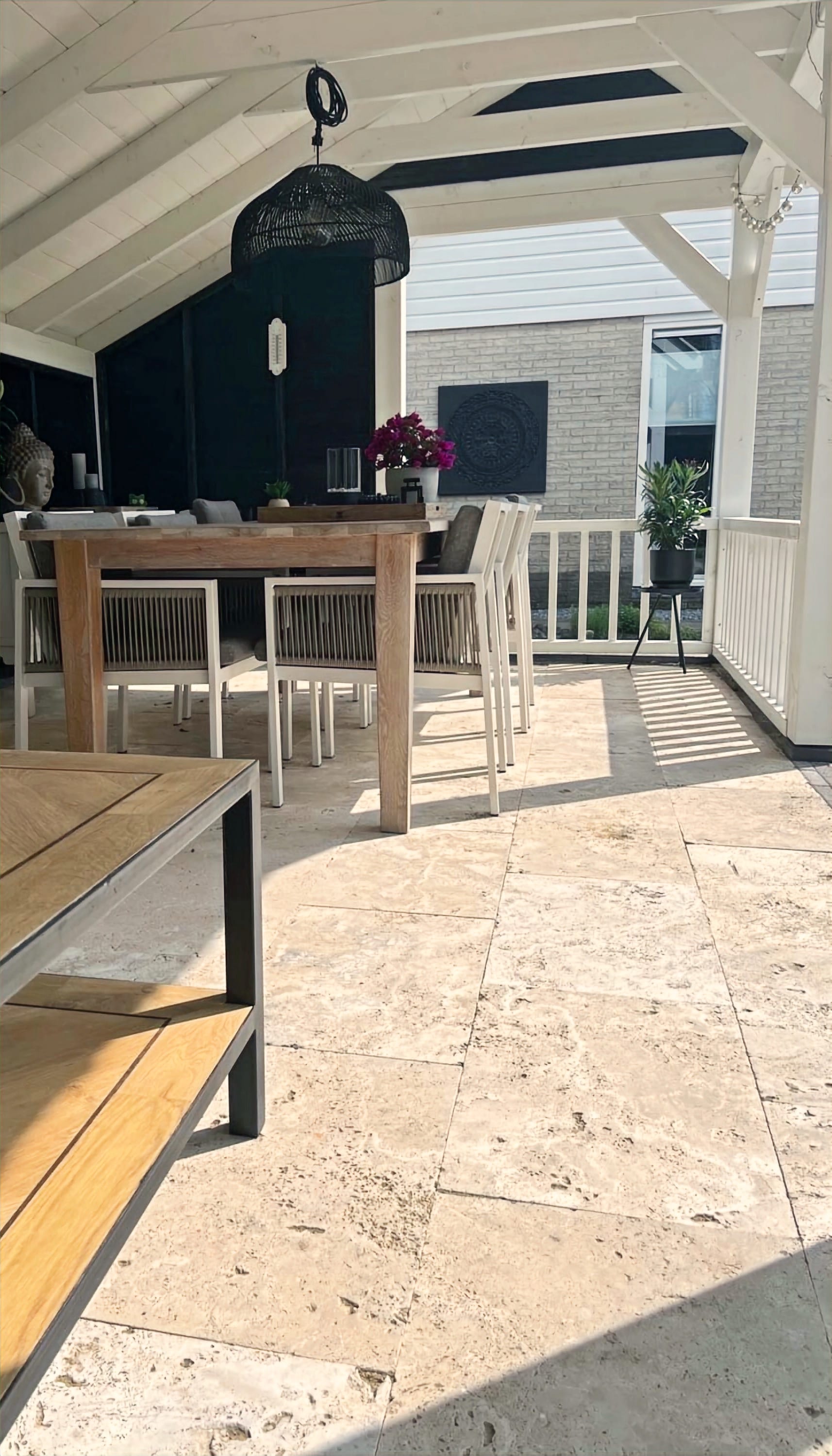 Overkapping met travertin terrastegels, eettafel en zicht op de tuin