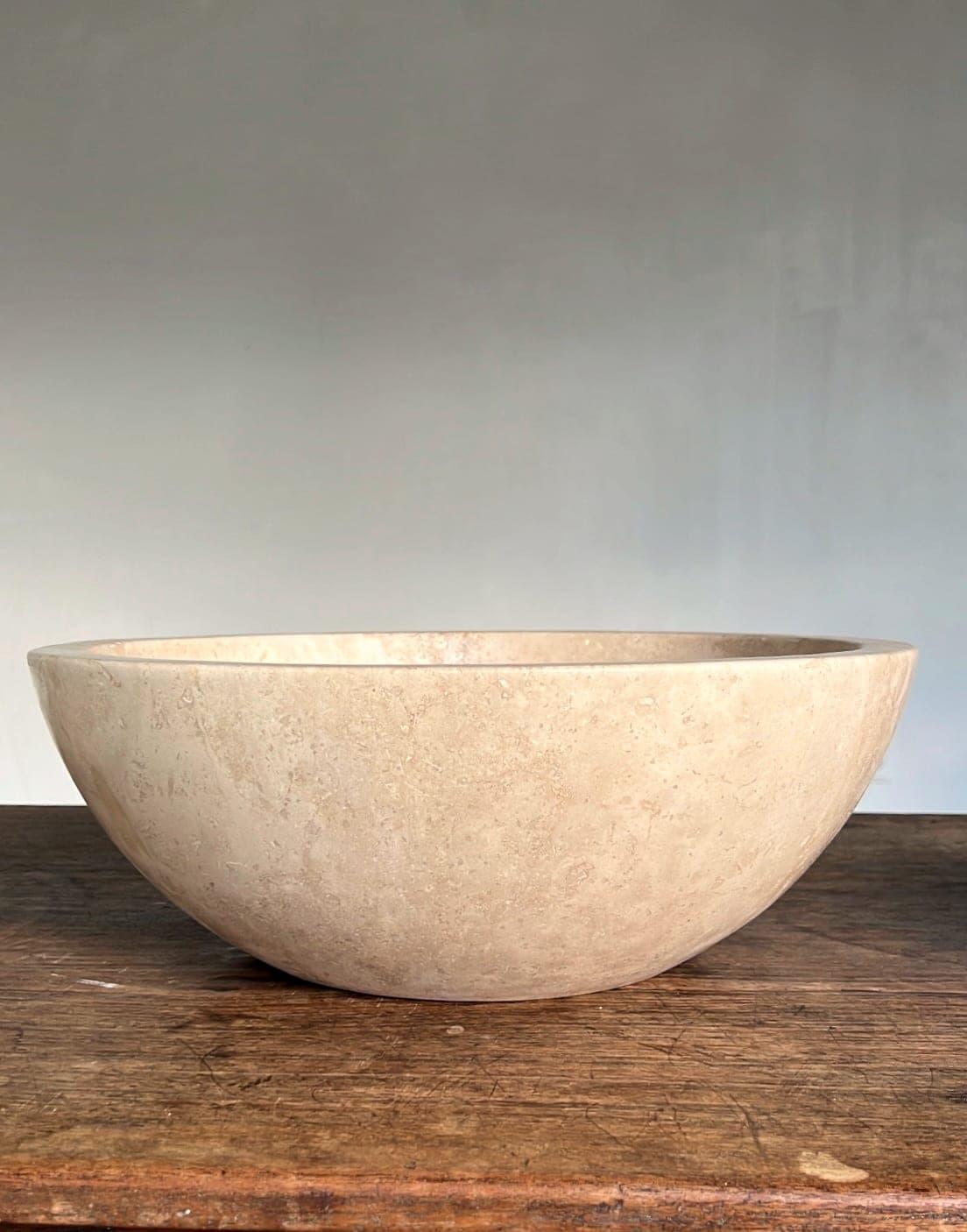 Vasque ronde en travertin ø40 cm, vue de côté sur une table en bois